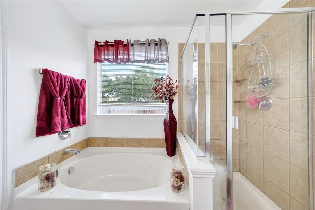 511 Chestnut Trail Forney, TX 75126 - Photo 27 of 32 White soaking tub with tiled surround, adjacent to a shower enclosure with glass doors and beige wall tiles