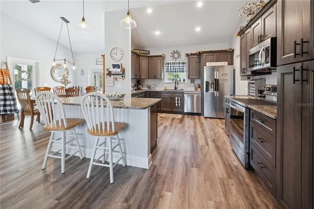 a kitchen with stainless steel appliances kitchen island granite countertop a table chairs stove a sink dishwasher and cabinets