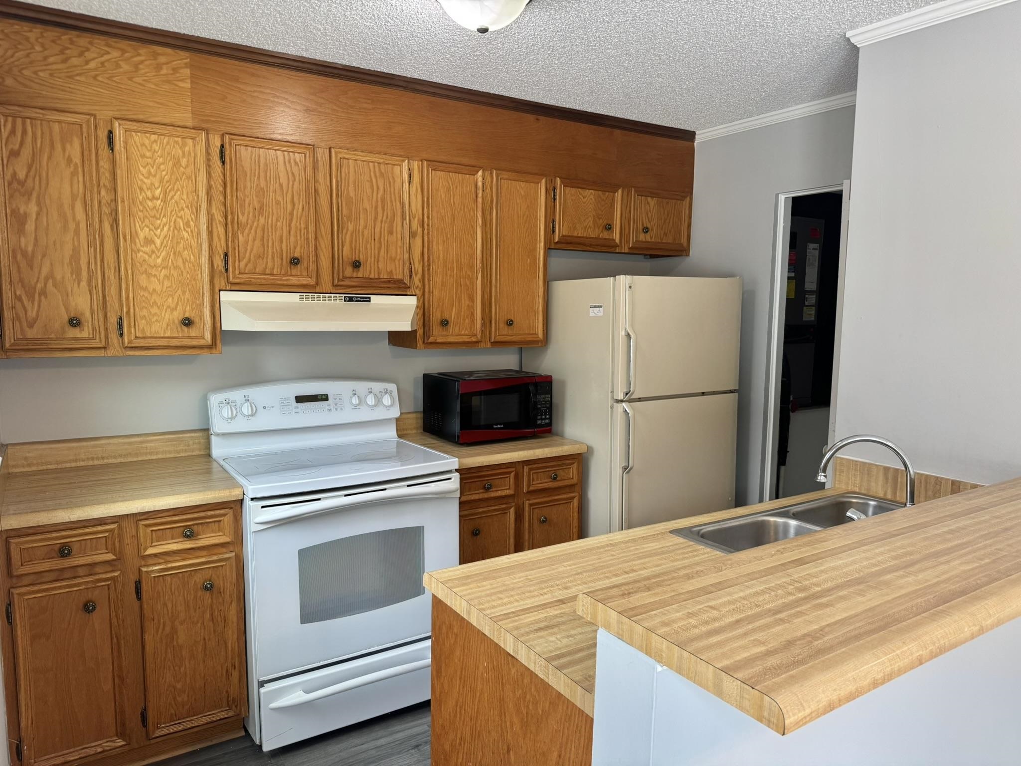 4115 Little River Road, Unit 10B Myrtle Beach, SC 29577 - Photo 11 of 31 Kitchen featuring white appliances, light countertops, a textured ceiling, brown cabinetry, and under cabinet range hood