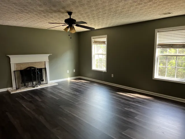 a view of an empty room with wooden floor fireplace and a window