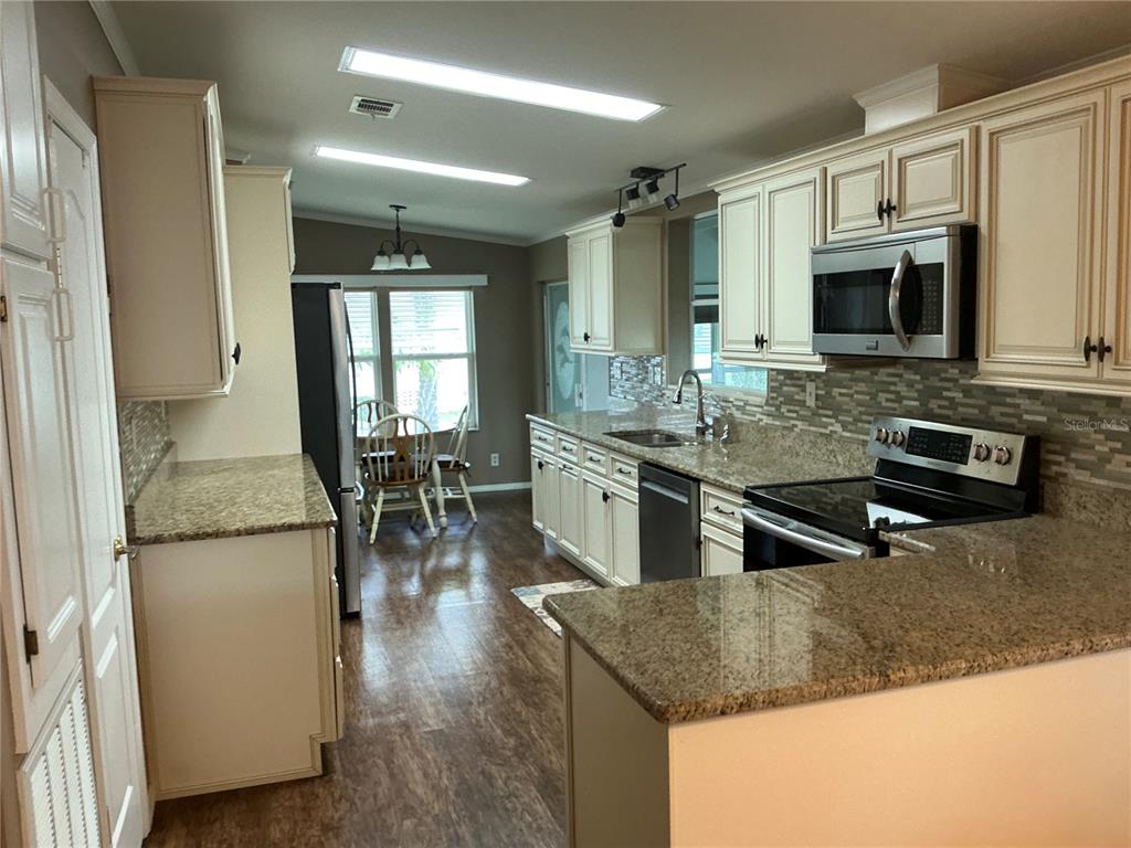236 Allies Pass, Unit 363 Frostproof, FL 33843 - Photo 47 of 51 a kitchen with stainless steel appliances granite countertop a refrigerator a stove a sink a dining table and chairs with wooden floor