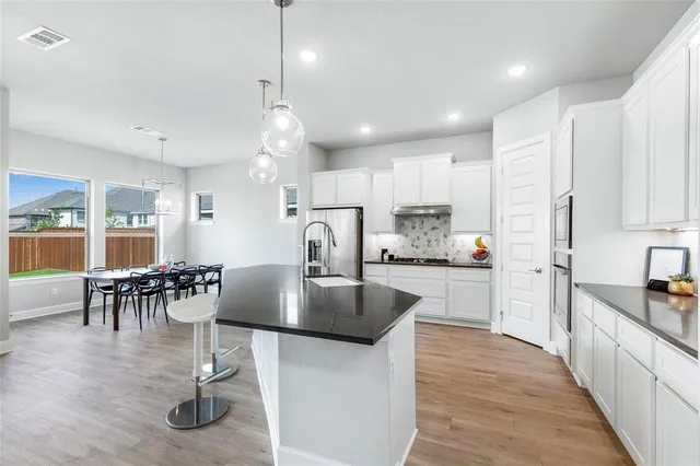 a kitchen with stainless steel appliances granite countertop a stove top oven a sink a dining table and chairs with wooden floor