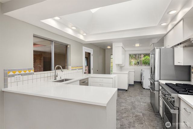 a large white kitchen with a stove a sink a counter space and living room view