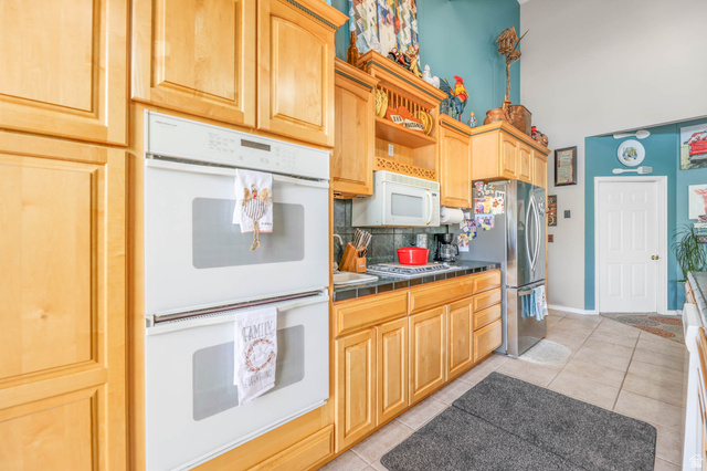 569 Elk Meadow Loop Tooele, UT 84074 - Photo 17 of 56 Kitchen with stainless steel appliances, light wood finish cabinets, backsplash, light tile patterned flooring, and tile countertops