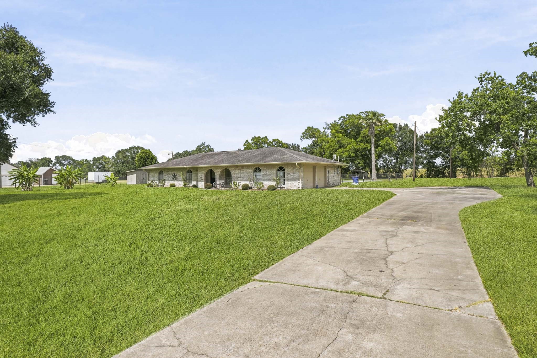 302 Country Road 893 Angleton, TX 77515 - Photo 5 of 26 Spacious home with a long driveway, nestled on a huge, well-maintained lawn. The house features a light brick exterior and arched windows, surrounded by mature trees, offering a serene, private setting.