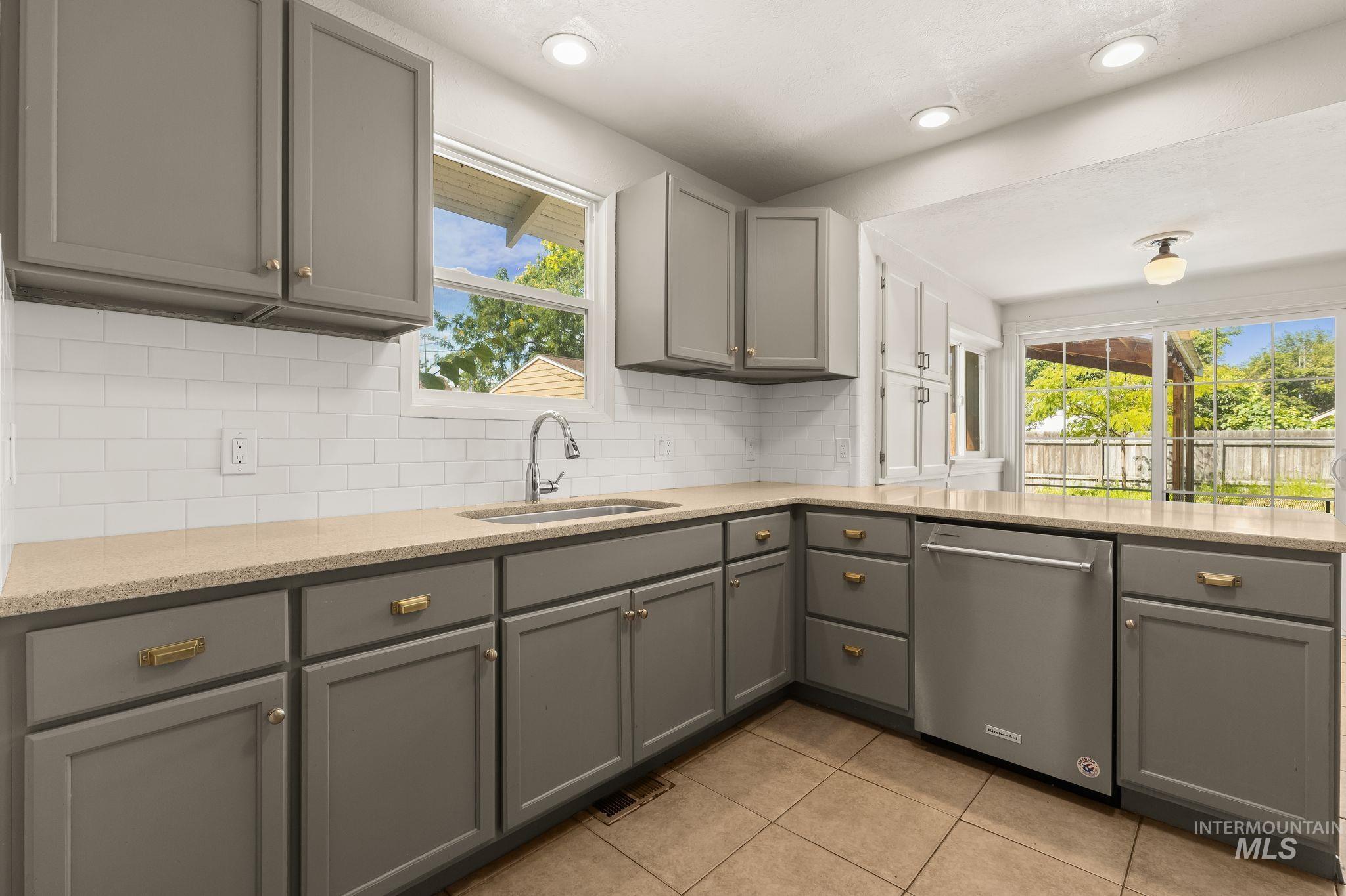 928 3rd Street Clarkston, WA 99403 - Photo 12 of 44 Kitchen featuring gray cabinetry with brass-tone hardware, a white subway tile backsplash, light-toned countertops, and a stainless steel dishwasher