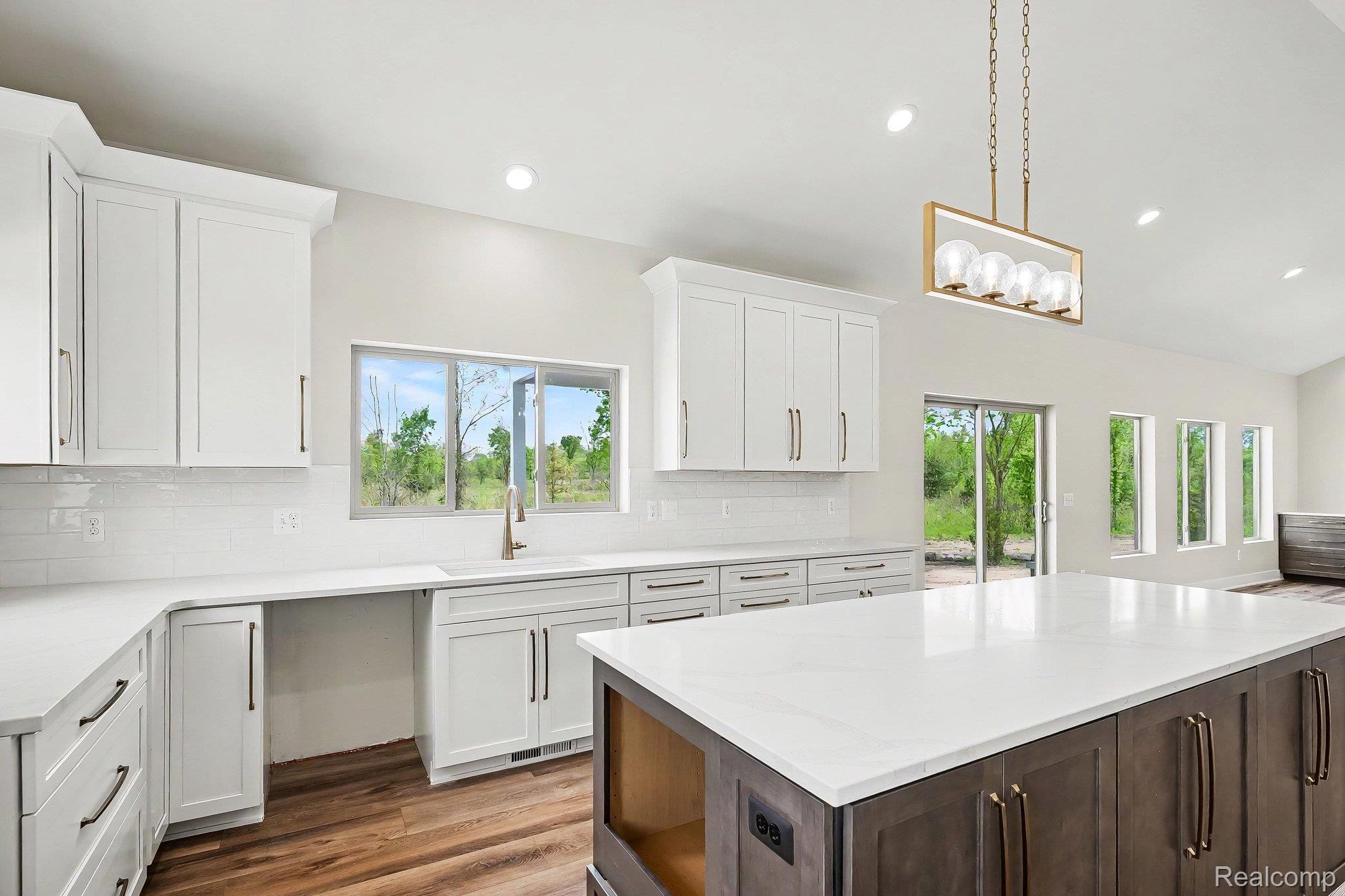 57560 Omo Road Ray, MI 48096 - Photo 15 of 44 Open-concept kitchen featuring an expansive center island with white countertop, white perimeter cabinetry, lvl flooring, and a contemporary linear chandelier