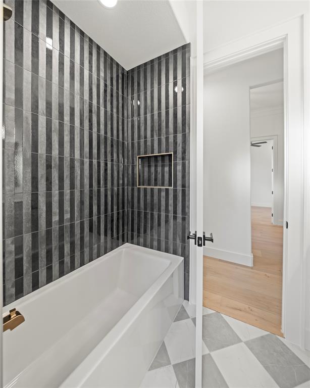 108 Bel Grand Road Haslet, TX 76052 - Photo 11 of 36 White soaking tub with gold-finish fixtures, set against a vertically-oriented striped tile shower surround featuring a recessed niche