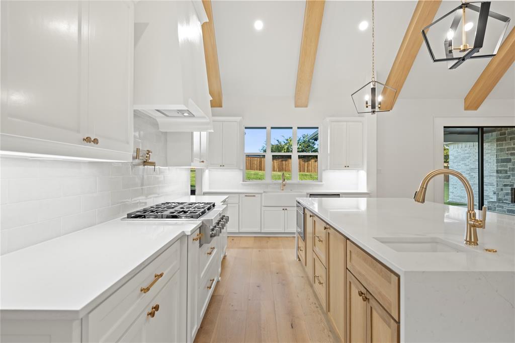 108 Bel Grand Road Haslet, TX 76052 - Photo 23 of 36 Spacious kitchen featuring vaulted ceilings with exposed wood beams, white cabinetry, a large kitchen island with integrated sink, stainless steel gas range, and wood-finish flooring