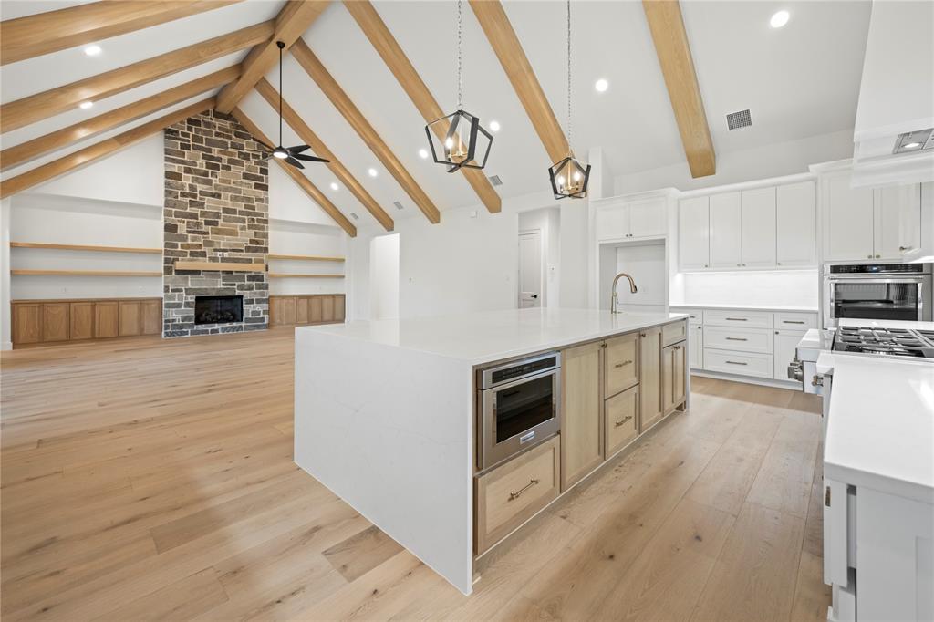 108 Bel Grand Road Haslet, TX 76052 - Photo 24 of 36 Open-concept kitchen and living area featuring vaulted ceilings with exposed wood beams, a stone-front fireplace, built-in shelving, a large central island with an integrated microwave, and stainless steel appliances
