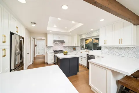 a open kitchen with stainless steel appliances kitchen island a sink dishwasher a refrigerator and white cabinets with wooden floor