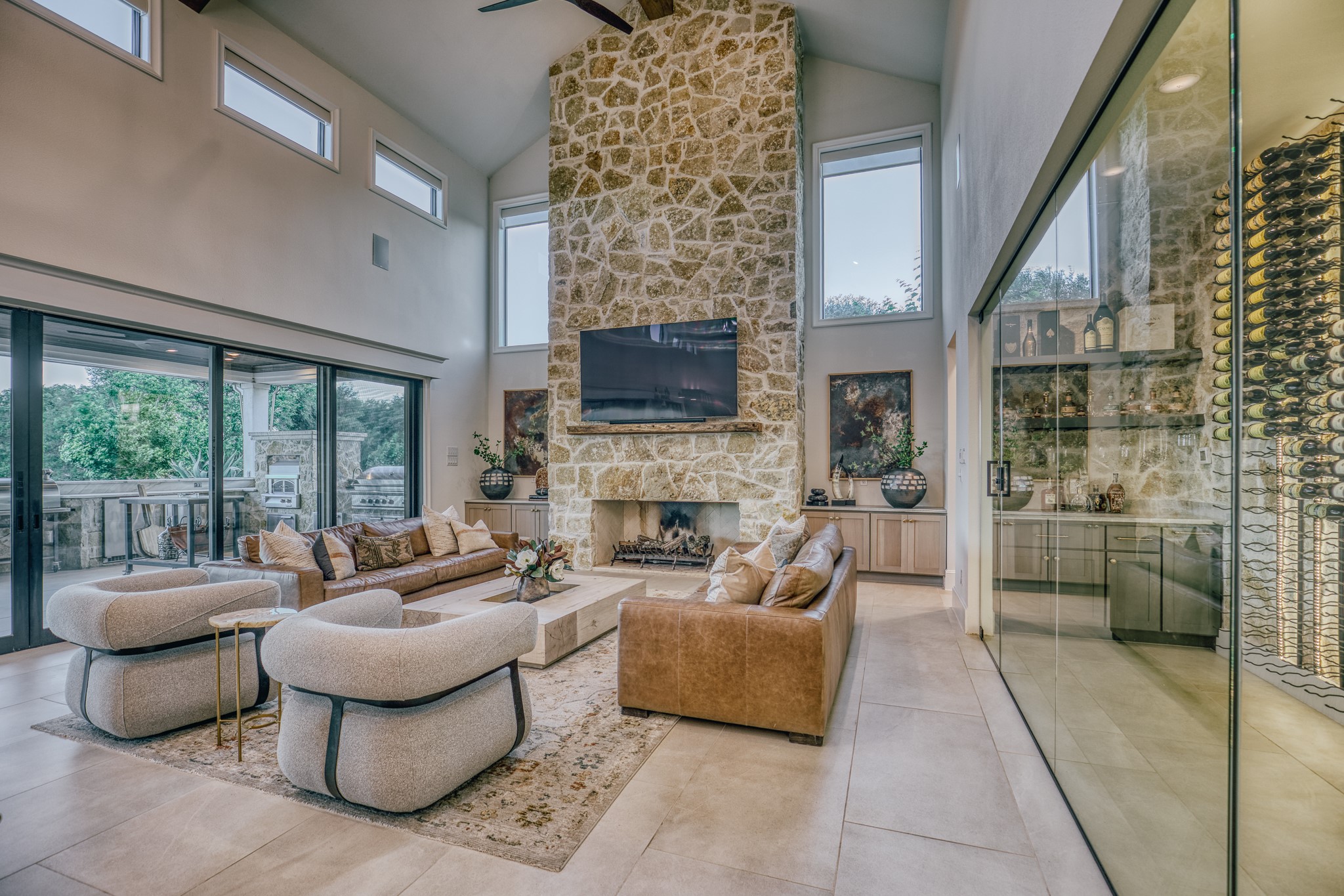 1034 Hilbun Road New Ulm, TX 78950 - Photo 18 of 49 Soaring vaulted ceilings with exposed beams, a floor-to-ceiling stone fireplace, climate-controlled wine room, and collapsible glass walls create seamless indoor-outdoor living and entertaining.