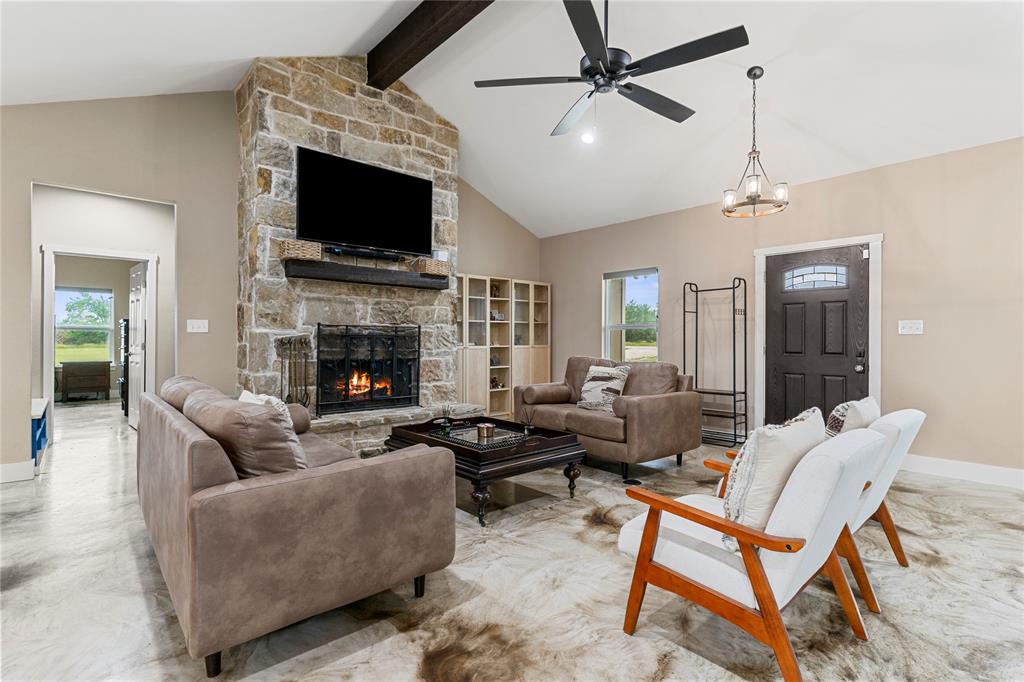 139 Kriston Lane Springtown, TX 76082 - Photo 6 of 39 Vaulted living space featuring a stone-clad fireplace with mantel, a dark wood ceiling beam, and a ceiling fan with integrated lighting