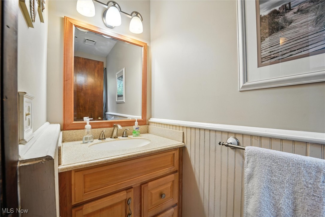 12120 Caves Road Chesterland, OH 44026 - Photo 6 of 50 Half bathroom featuring vanity, a wainscoted wall, and wood walls
