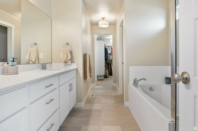 1295 East Granite Peak Road Eagle Mountain, UT 84005 - Photo 18 of 35 Bathroom featuring a double vanity with white cabinetry and a light-toned countertop, a built-in soaking tub, and tile flooring