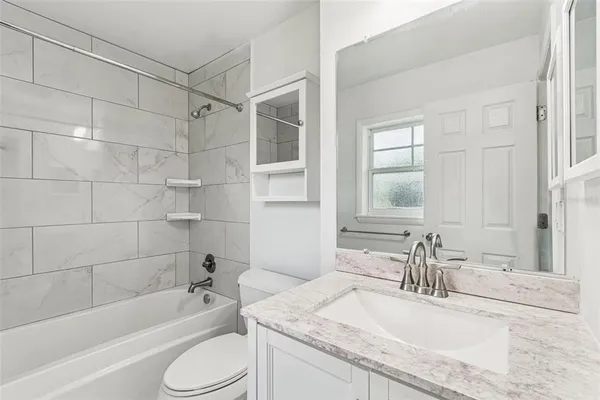 a bathroom with a granite countertop bathtub shower sink vanity mirror and toilet