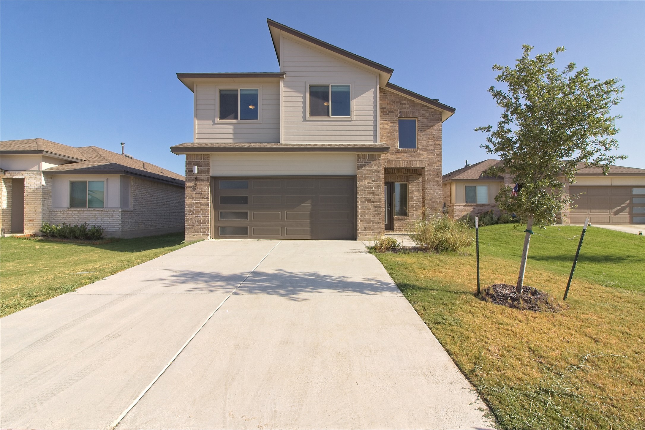 Modern home featuring brick siding, a front yard, an attached garage, and driveway