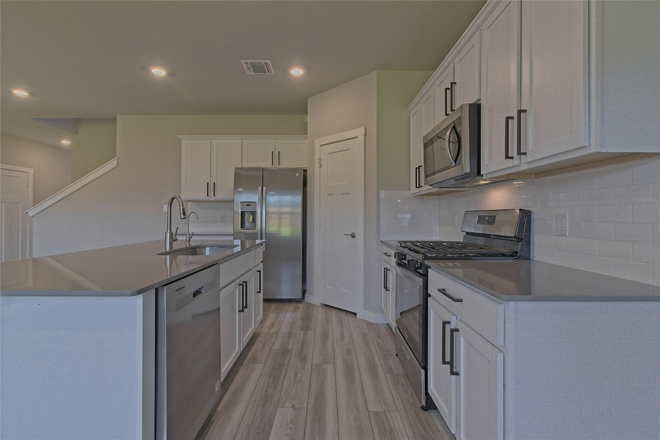 425 Coda Crossing Georgetown, TX 78633 - Photo 12 of 36 Kitchen with stainless steel appliances, white cabinets, light wood-type flooring, a kitchen island with sink, and light stone counters