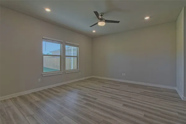 an empty room with wooden floor chandelier fan and windows