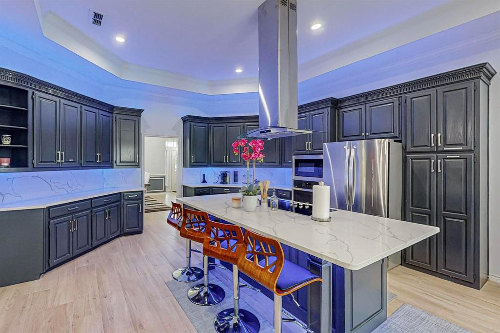 4908 Glenwood Lane Anna, TX 75409 - Photo 6 of 34 Kitchen with a tray ceiling, light stone counters, a breakfast bar area, light wood finished floors, and crown molding