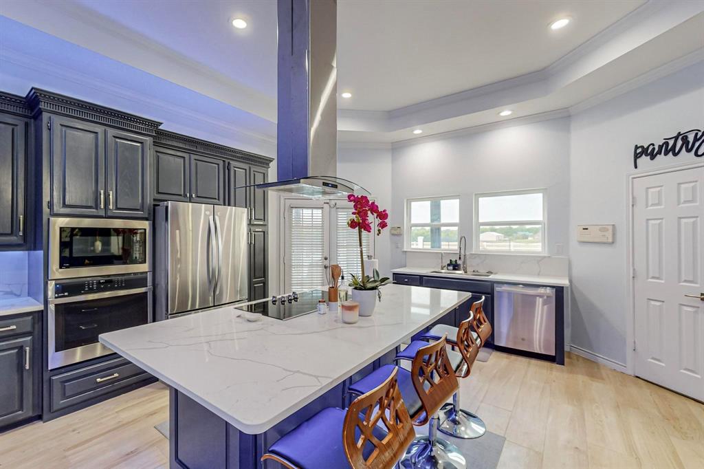 4908 Glenwood Lane Anna, TX 75409 - Photo 7 of 34 Kitchen with a tray ceiling, light wood-style floors, appliances with stainless steel finishes, light stone counters, and a center island
