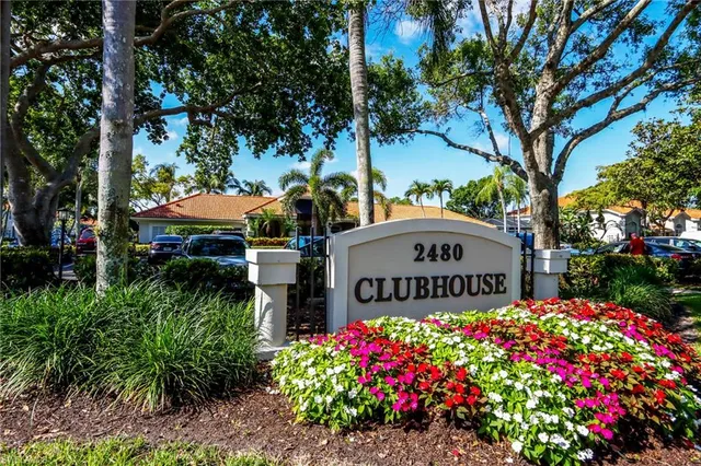 a view of sign board with flower plants and large trees