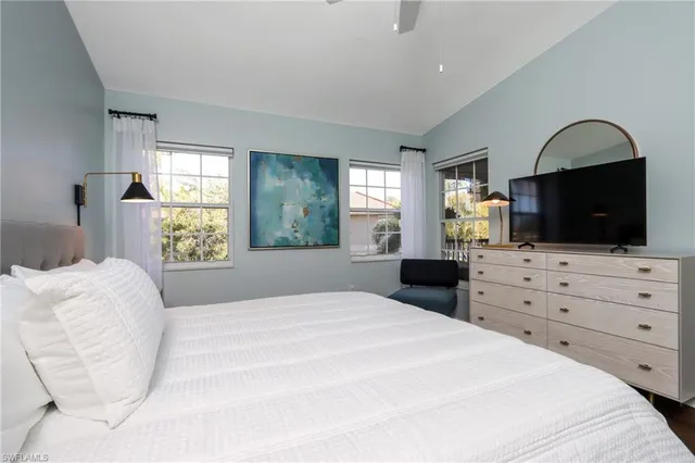 a bedroom with a large bed and a flat tv screen on dresser next to a window