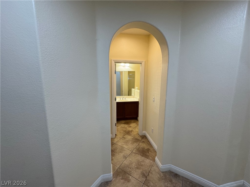 1333 Jamesbury Road Las Vegas, NV 89135 - Photo 4 of 43 An arched hallway leads to a well-appointed bathroom featuring a single vanity and tiled flooring.