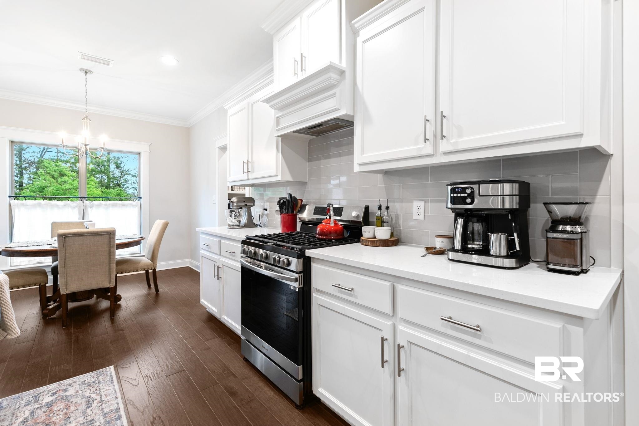 13233 Ibis Boulevard Daphne, AL 36527 - Photo 18 of 100 Kitchen and dining area featuring white shaker-style cabinetry, stainless steel appliances, quartz countertops, a grey subway tile backsplash, and wood-finish flooring