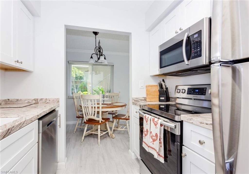 Kitchen featuring stainless steel appliances, ornamental molding, white cabinetry, and light stone counters