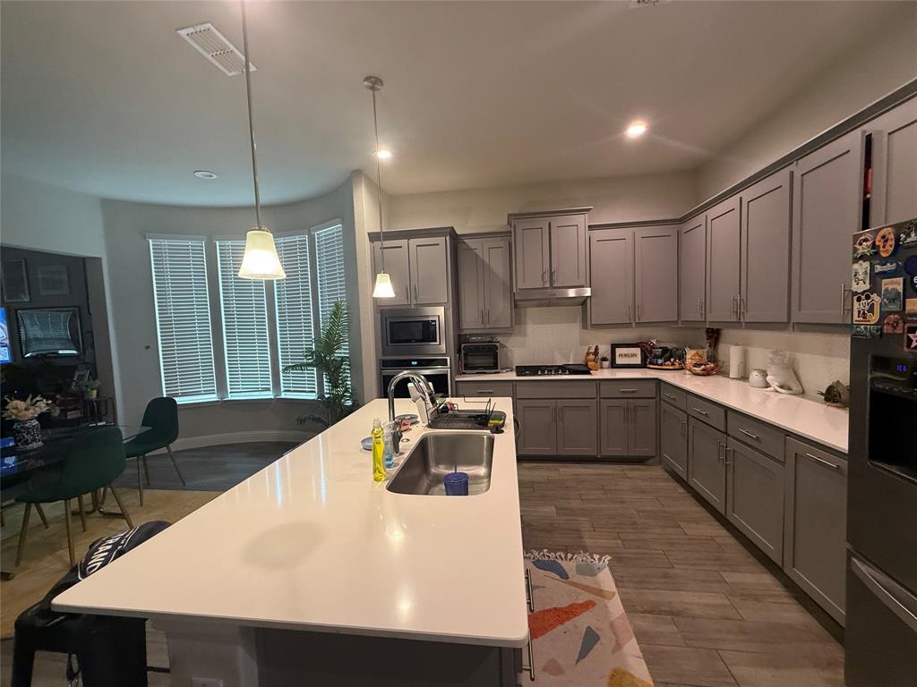 1121 Knightsbridge Road Argyle, TX 76226 - Photo 4 of 7 Kitchen featuring gray cabinets, stainless steel appliances, light wood-style flooring, and decorative light fixtures
