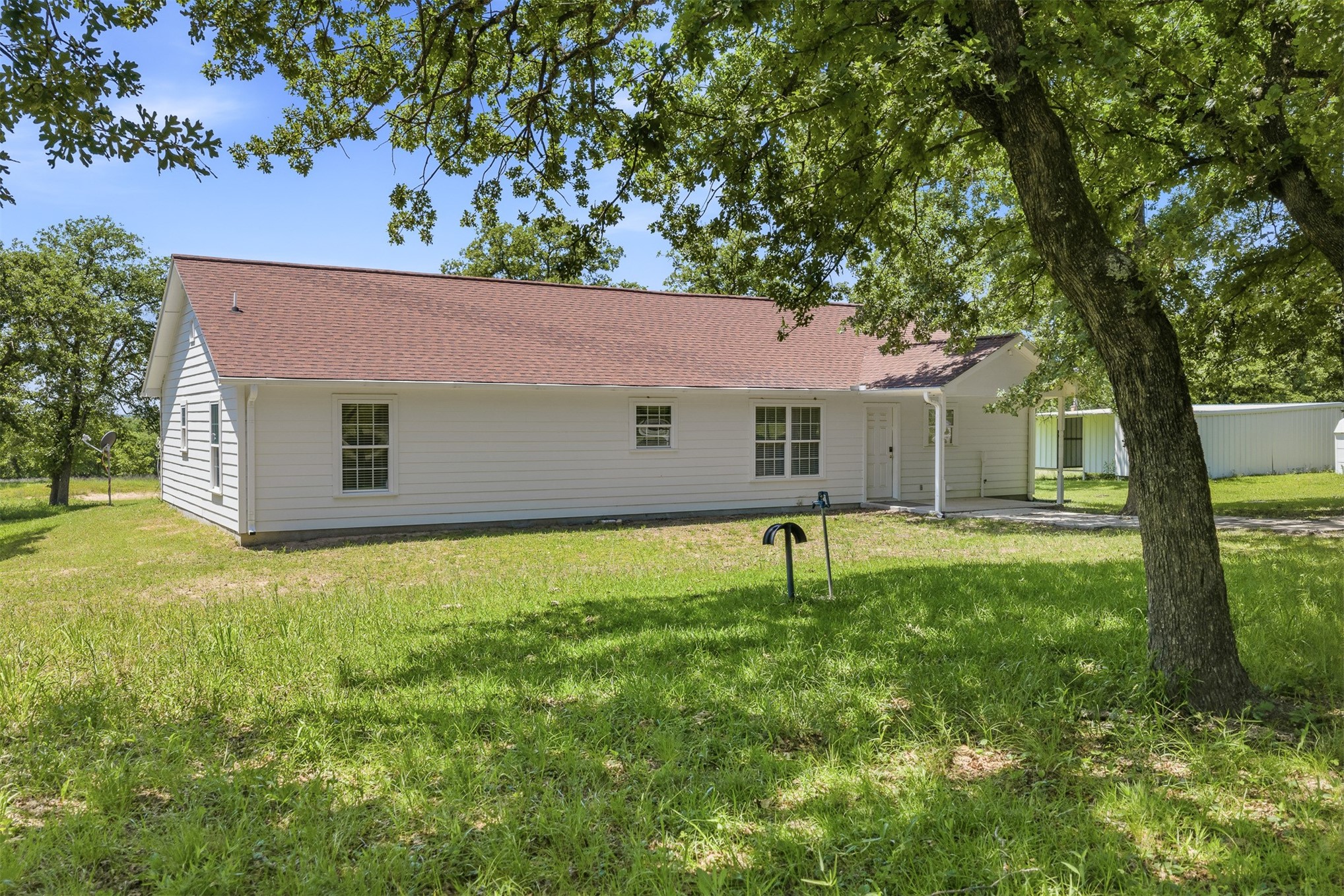 831 Barrons Ridge Wilson, OK 73463 - Photo 28 of 47 White siding exterior with a red shingle roof, featuring multiple windows with grid patterns, a covered entry, and a covered carport