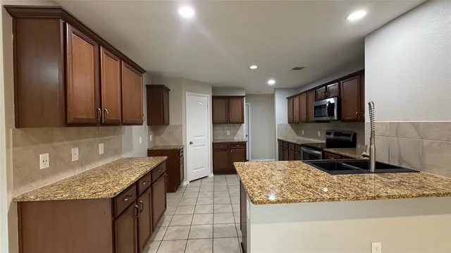 a kitchen with granite countertop stainless steel appliances a sink a stove top oven a counter space and cabinets