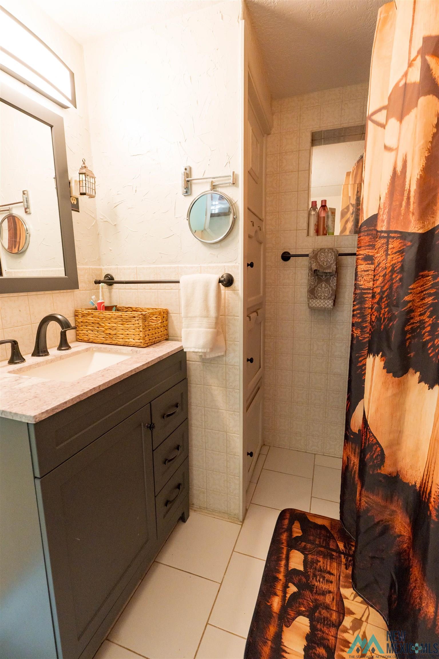 3 Wimsatt Road Cloudcroft, NM 88317 - Photo 19 of 41 Bathroom featuring vanity, light tile patterned flooring, tile walls, a shower with shower curtain, and a textured ceiling
