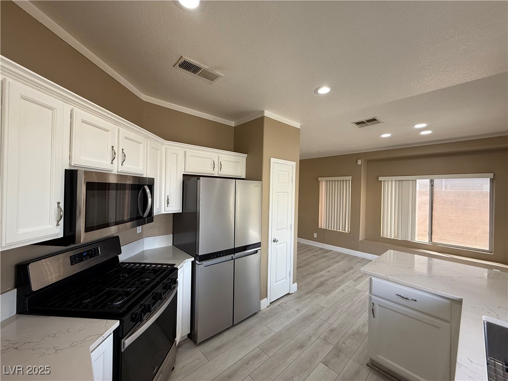 7062 Russell Ranch Avenue Las Vegas, NV 89113 - Photo 19 of 32 Kitchen with visible vents, white cabinets, light wood-style floors, and stainless steel appliances