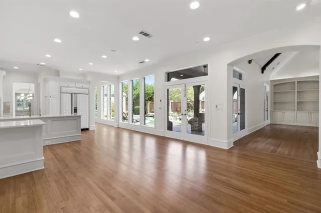 a view of an empty room with wooden floor and a kitchen