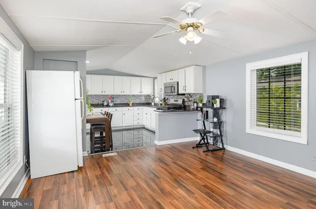 a kitchen with kitchen island a stove a refrigerator cabinets a dining table and chairs with wooden floor