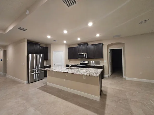 a large kitchen with kitchen island a large counter top stainless steel appliances and cabinets