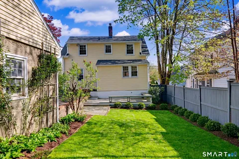 a view of a white house with a big yard and potted plants and a large tree