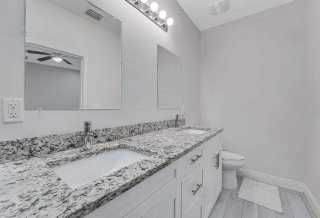 a bathroom with a granite countertop sink a toilet and a mirror