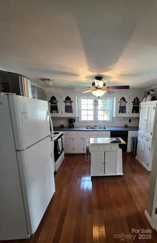 a kitchen with granite countertop a refrigerator a sink dishwasher a stove and white cabinets with wooden floor