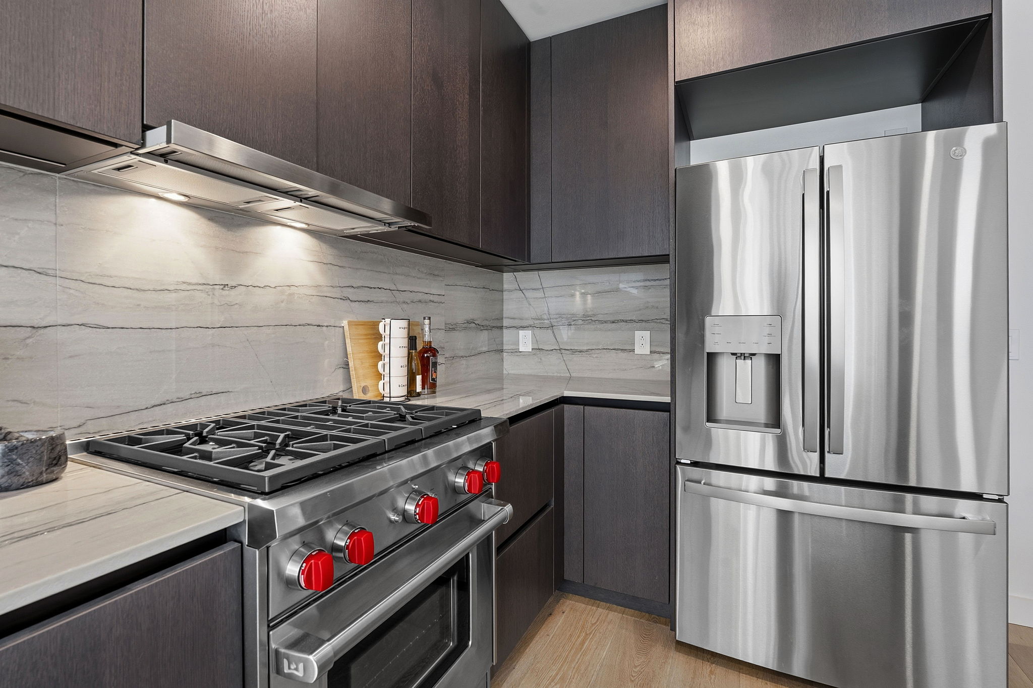 610 Davis Street, Unit 3004 Austin, TX 78701 - Photo 12 of 40 Kitchen featuring stainless steel appliances, modern cabinets, range hood, light wood-style flooring, and light stone counters