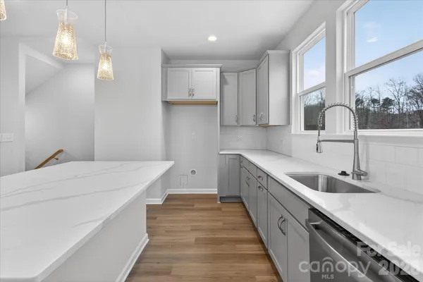 a kitchen with a sink dishwasher and white cabinets with wooden floor
