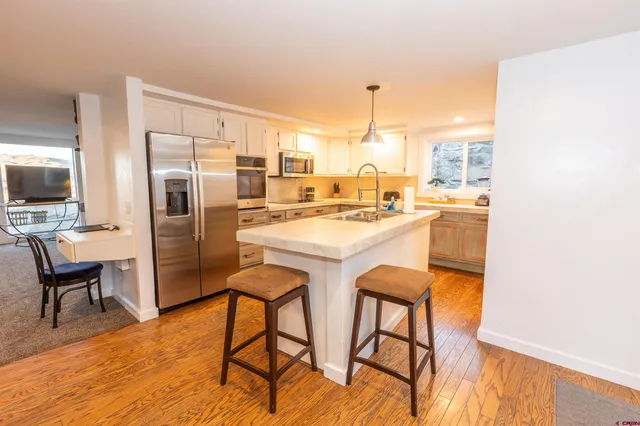 a kitchen with stainless steel appliances a dining table chairs refrigerator and sink