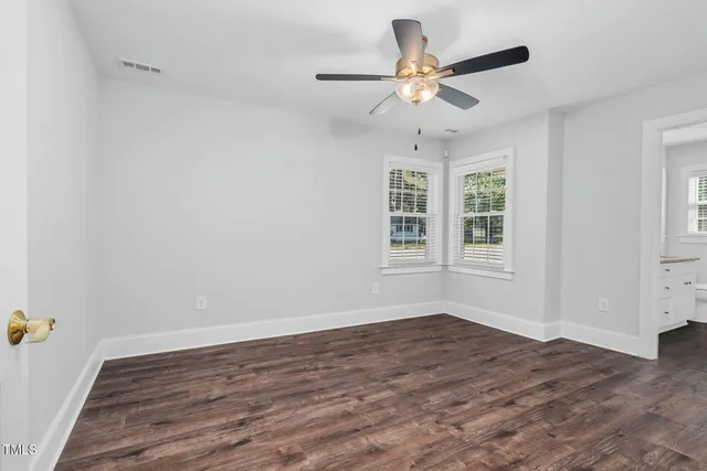 an empty room with wooden floor fan and windows