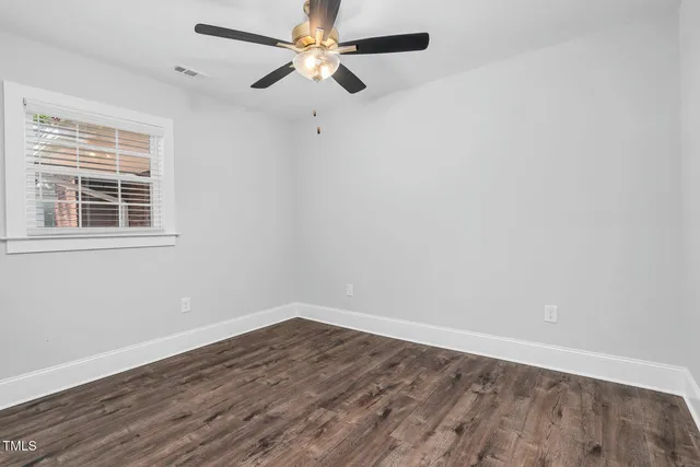 an empty room with wooden floor fan and windows