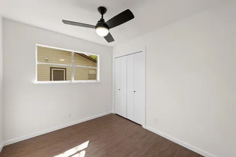 a view of an empty room with wooden floor and a ceiling fan
