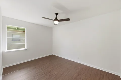 an empty room with wooden floor ceiling fan and window