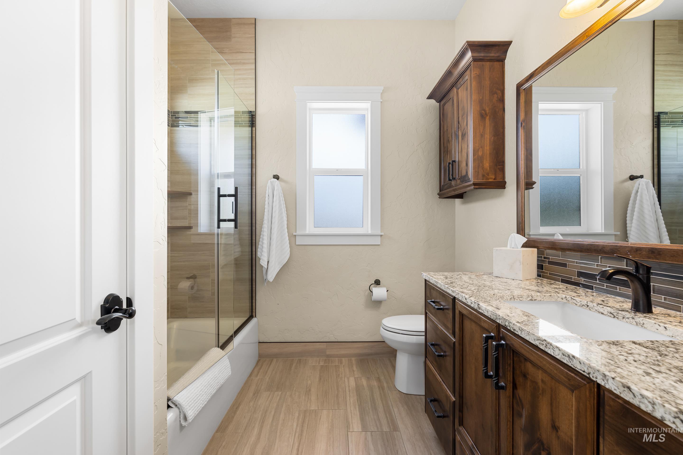 9819 Foothill Road Middleton, ID 83644 - Photo 30 of 49 Bathroom with vanity, combined bath / shower with glass door, backsplash, and wood finished floors