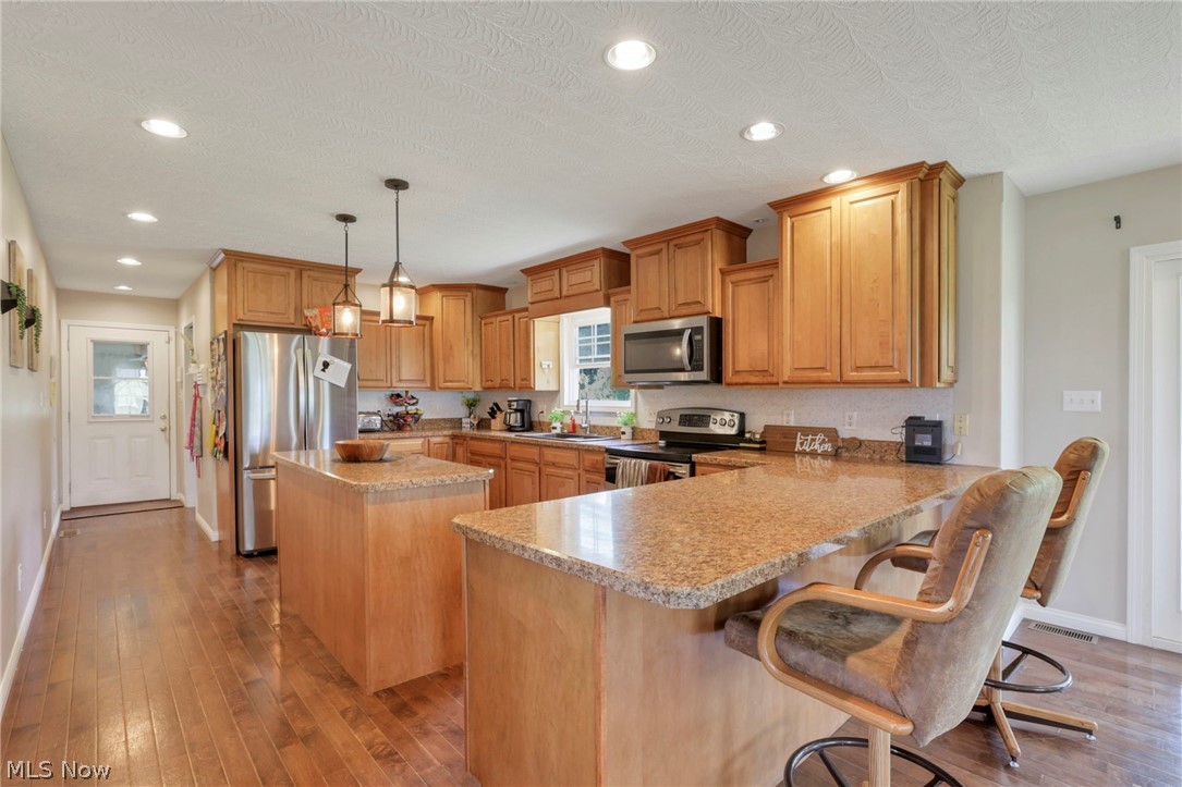 3483 Cooper Road Cumberland, OH 43732 - Photo 9 of 50 Kitchen featuring hanging light fixtures, appliances with stainless steel finishes, hardwood / wood-style floors, and a breakfast bar